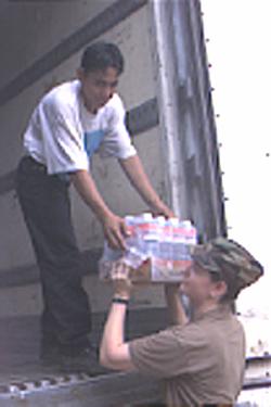  Winston Hernandez, Guatemalan KP, hands Spec. Kimberly Row, 308th Quartermaster Company, Washington, Iowa, a case of bottled water from the refrigerated trailer. Bottled water is used for all cooking at base camp Motagua during the humanitarian mission, New Horizons '99.
